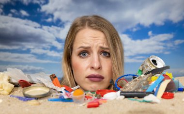 Kafasına kadar plaja gömülü, çöp ve plastik atıklarla dolu güzel bir kadının hareketlerini durdurun.