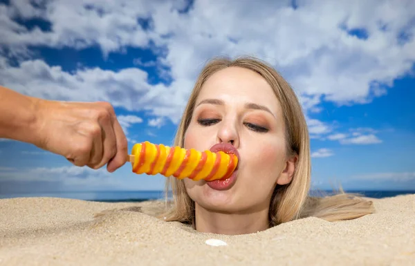 一个漂亮的女人把头埋在海滩上 舔着另一只手捧着的棒棒糖 — 图库照片