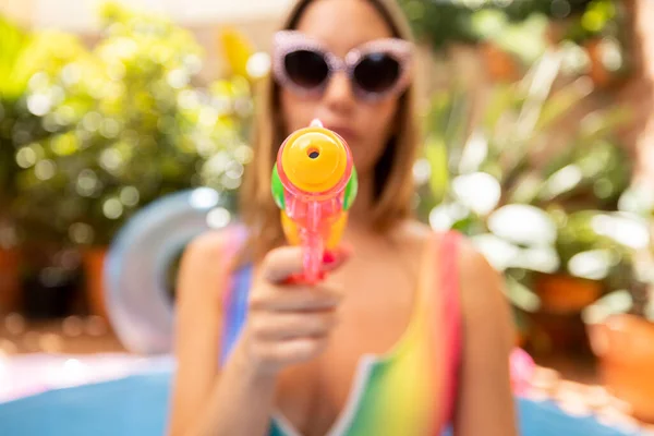 A pretty woman in bikini with a water pistol in a paddling pool