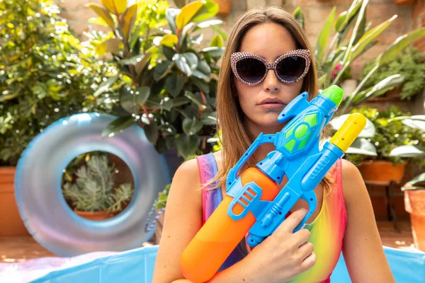 A pretty woman in bikini with a water pistol in a paddling pool