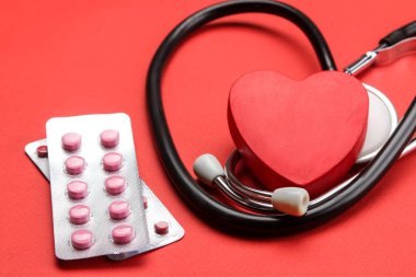 Kırmızı arka planda steteskop ve kırmızı bir kalp. Kalp sağlığı ve sağlık hizmetleri.