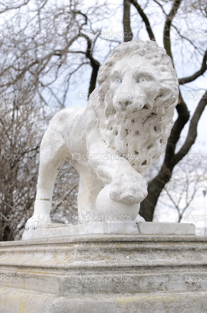 Stone lion sculpture upon naked trees background
