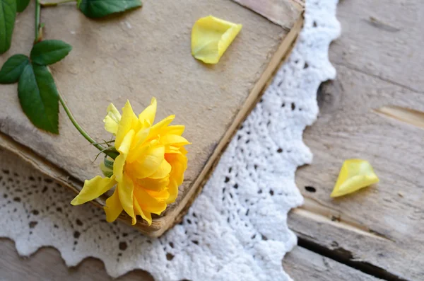 Yellow rose laying upon vintage book on lace doily — Stock Photo, Image