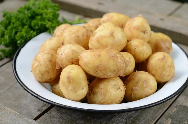 Young potato in metal bowl on wooden background — Stock Photo, Image