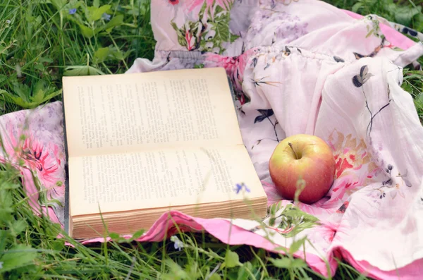 Maçã e livro aberto em grama verde — Fotografia de Stock