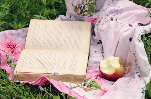 Maçã e livro aberto em grama verde — Fotografia de Stock
