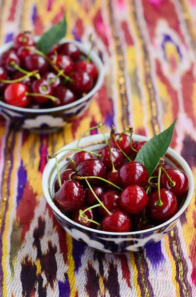 Ripe cherry in oriental bowls on bright ethnic tablecloth — Stock Photo, Image