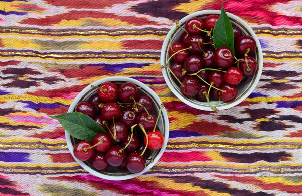 Bowls with ripe cherry over bright oriental tablecloth — Stock Photo, Image