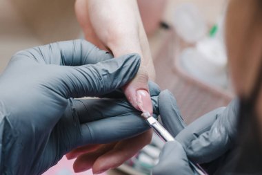 Gri eldivenli manikürcü tırnaklarını pembe jölelerle kaplıyor.