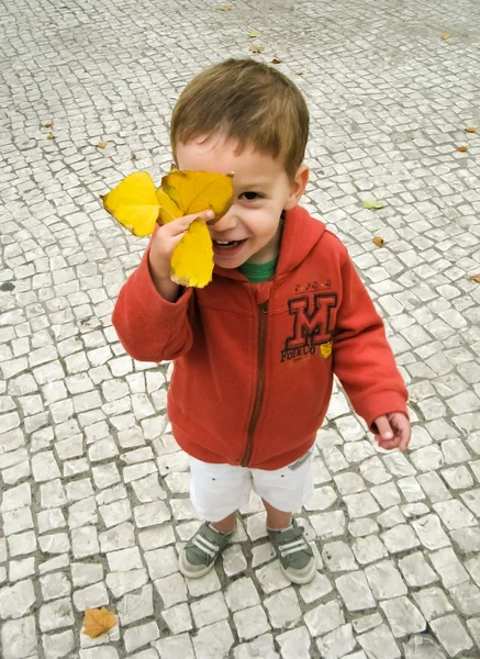 Улыбающийся ребенок покрывает лицо осенним листом — стоковое фото
