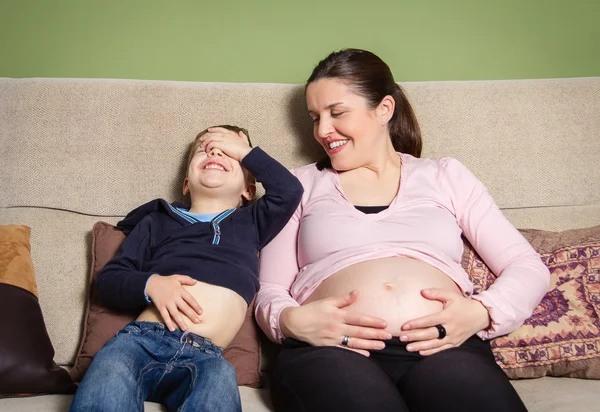 Pregnant mother and son laughing and comparing bellies — Stock Photo, Image