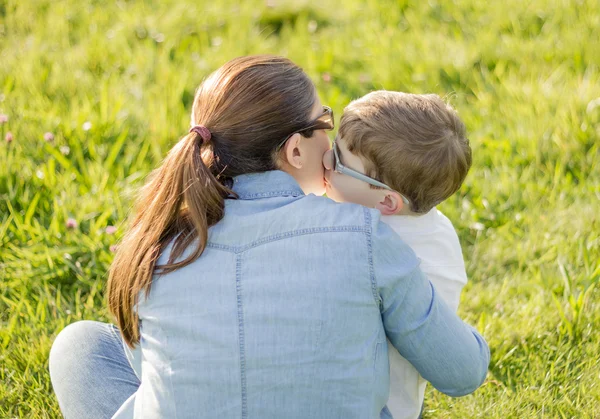 Cute son kissing to his mother sitting in a field — Stock Photo, Image