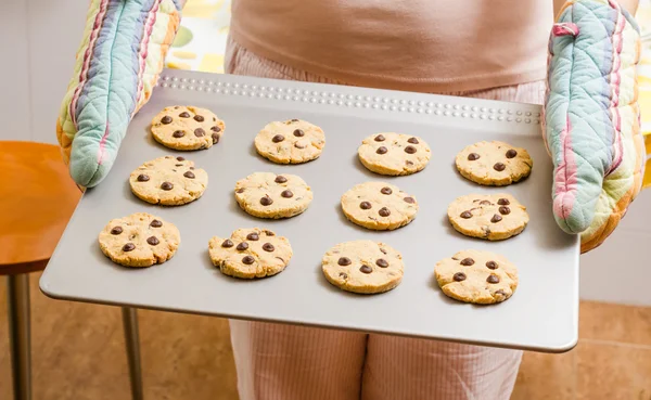 Donna in possesso di un vassoio con biscotti al forno con guanti da cucina — Foto Stock