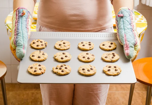 Donna in possesso di un vassoio con biscotti al forno con guanti da cucina — Foto Stock