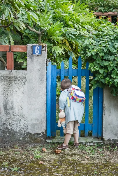 Nieuwsgierig school jongen op zoek door de houten hek — Stockfoto