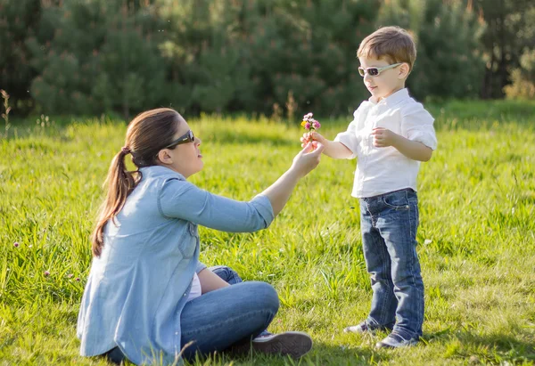 Son giving a bouquet of flowers to his pregnant mother in a fiel — Stock Photo, Image