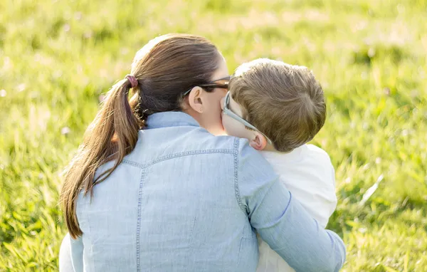 Cute son kissing to his mother sitting in a field — Stock Photo, Image