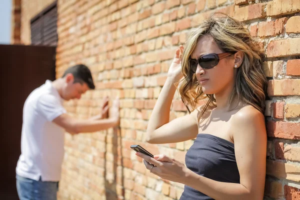 Boos vrouw op zoek telefoon en man die zich voordeed op de muur — Stockfoto