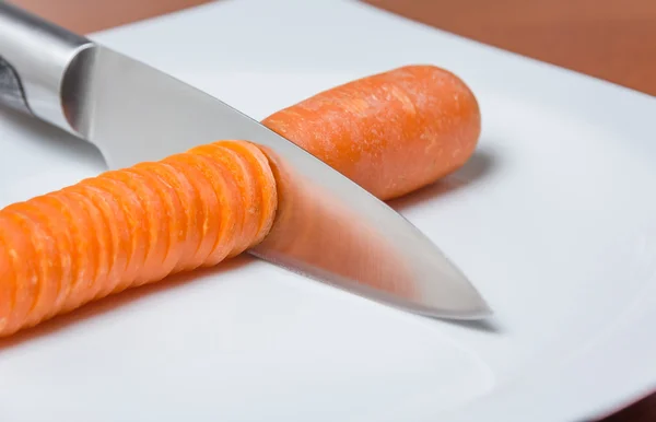 Couteau tranchant la carotte dans une assiette blanche sur la table — Photo