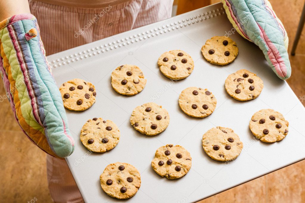 Woman with gloves holding a baked cookies tray