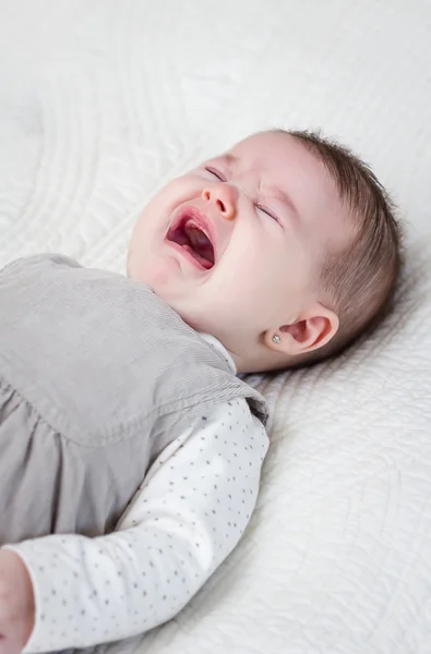 Bebê menina chorando sobre a cama branca — Fotografia de Stock