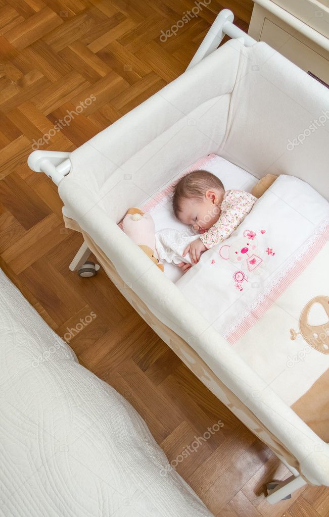 Baby girl sleeping in a cot with pacifier and toy