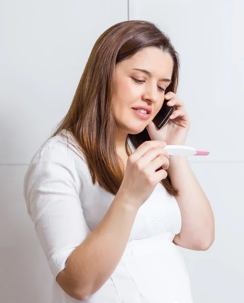Terhességi teszt és a telefonon beszél a nő — Stock Fotó