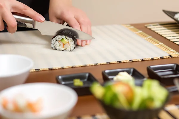 Крупный план женщины-повара, которая режет японский суши-ролл — стоковое фото