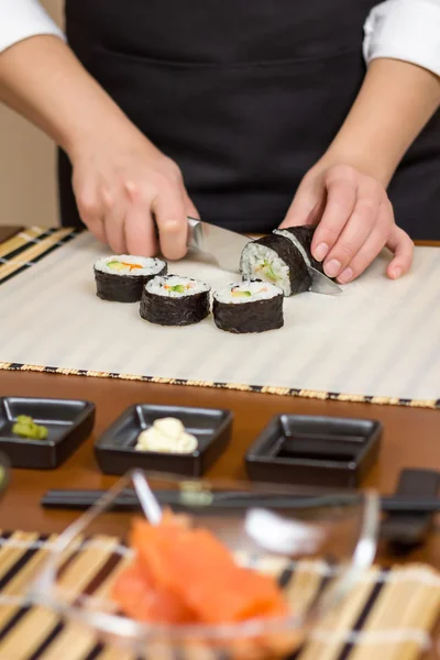 Крупный план женщины-повара, которая режет японский суши-ролл — стоковое фото