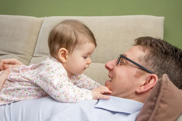 Bebê bonito brincando com seu pai feliz em um sofá — Fotografia de Stock