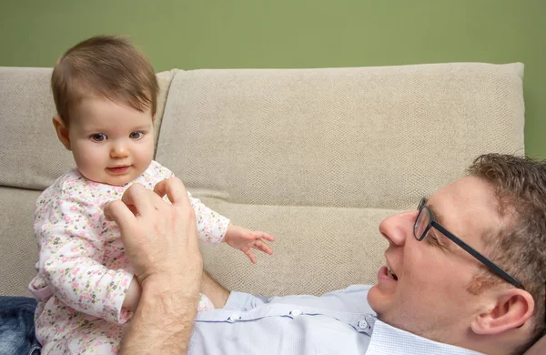 Pai feliz brincando com bebê bonito em um sofá — Fotografia de Stock