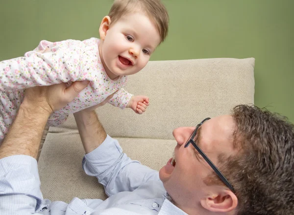 Bebê bonito brincando com seu pai feliz em um sofá — Fotografia de Stock