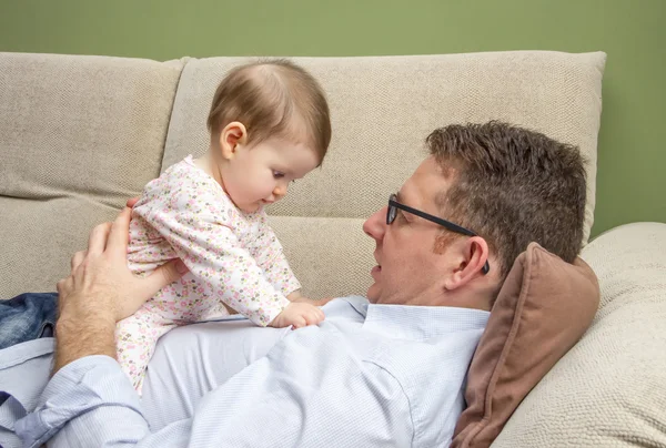 Pai feliz brincando com bebê bonito em um sofá — Fotografia de Stock