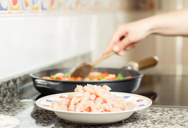 Raw chiken dish and female cooking in a pan — Stock Photo, Image