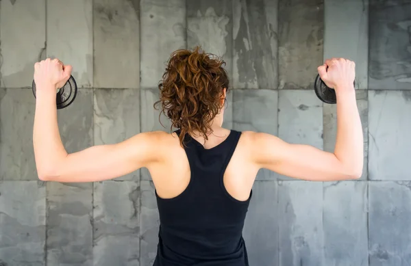 Back view of young girl lifting dumbbell discs — Stock Photo, Image