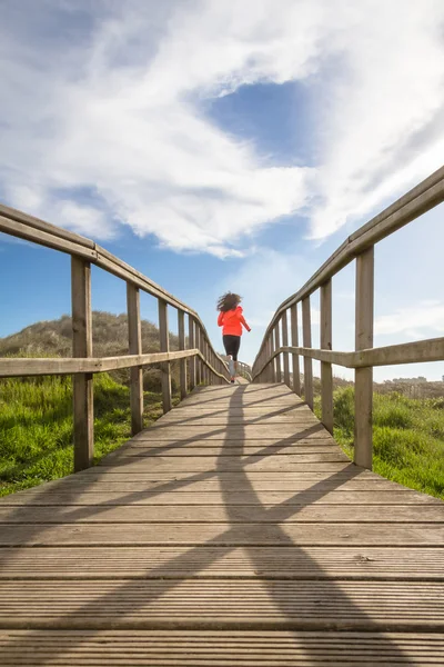 Back view of girl running in a wood boardwalk — Stock Photo, Image