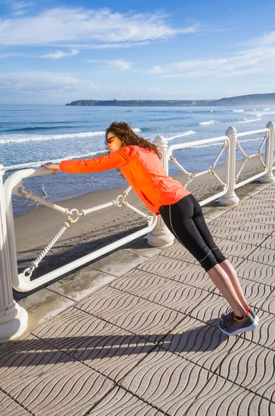 Chica joven calentándose antes de correr en un paseo marítimo — Foto de Stock