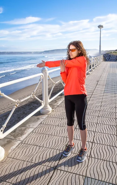 Chica joven calentándose antes de correr en un paseo marítimo — Foto de Stock