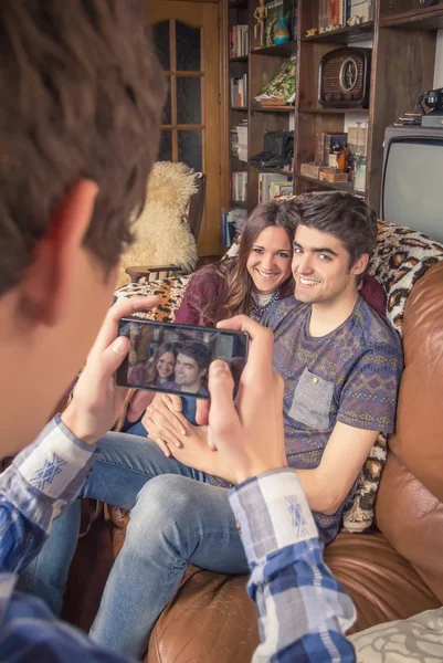 Friend taking photos to teenage couple on a sofa — Stock Photo, Image