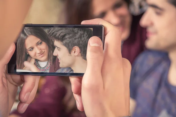 Boy hands taking photos to teenage couple on sofa — Stock Photo, Image