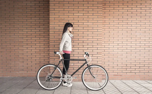 Sportive žena s fixie kolo přes cihlovou zeď — Stock fotografie