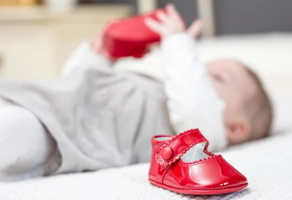 Dětské červené boty a dítě hraje na pozadí — Stock fotografie