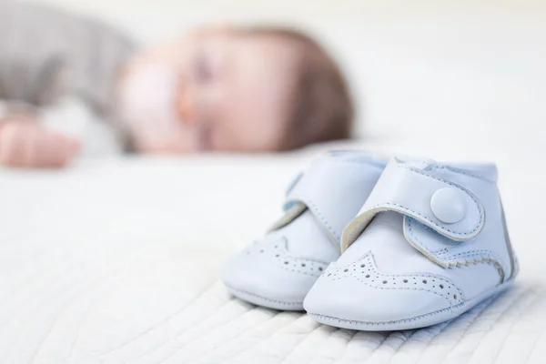 Baby blue shoes and babe sleeping on background — Stock Photo, Image