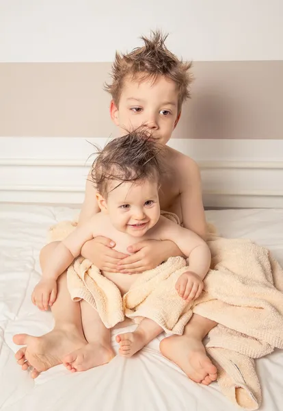 Menino e bebê com cabelo molhado sob toalhas sobre uma cama — Fotografia de Stock