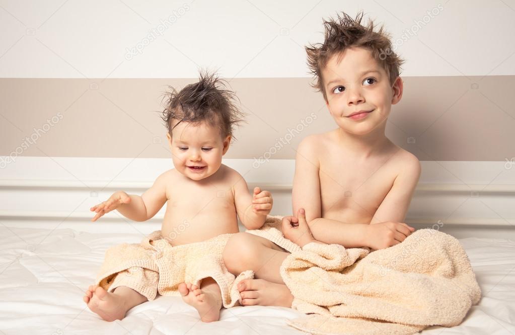 Boy and baby with wet hair under towels over a bed