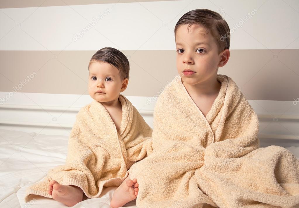 Sweet boy and little girl under towels over a bed