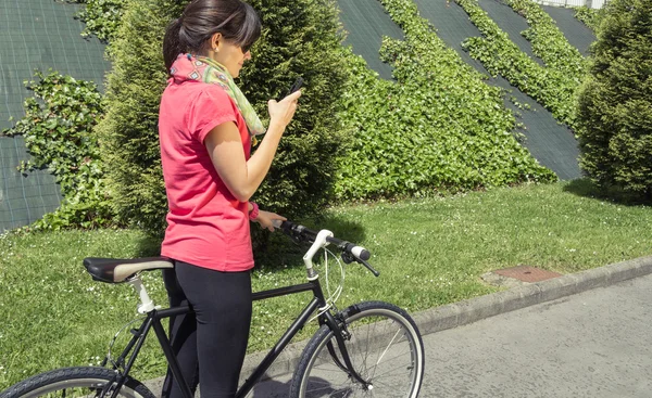 Спортивна жінка з фіксованим велосипедом дивиться смартфон — стокове фото