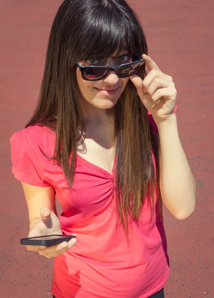 Jeune femme avec téléphone regardant par-dessus ses lunettes de soleil — Photo