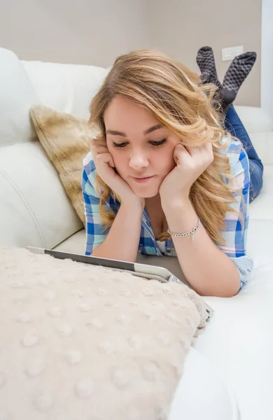 Beautiful teenager using tablet pc liying on sofa — Stock Photo, Image