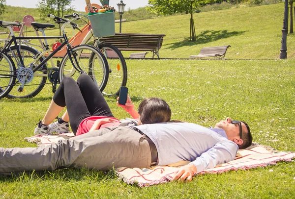 Девушка с помощью смартфона лежит над мужчиной в парке — стоковое фото